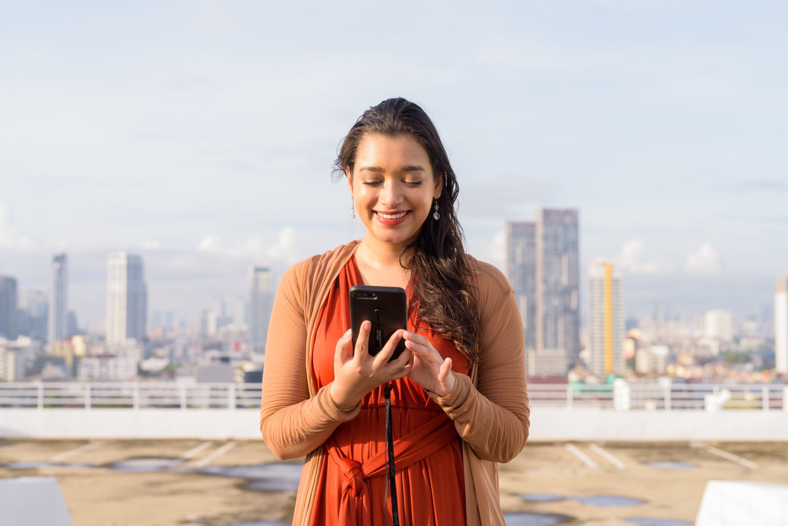 happy young beautiful indian woman using phone against view city