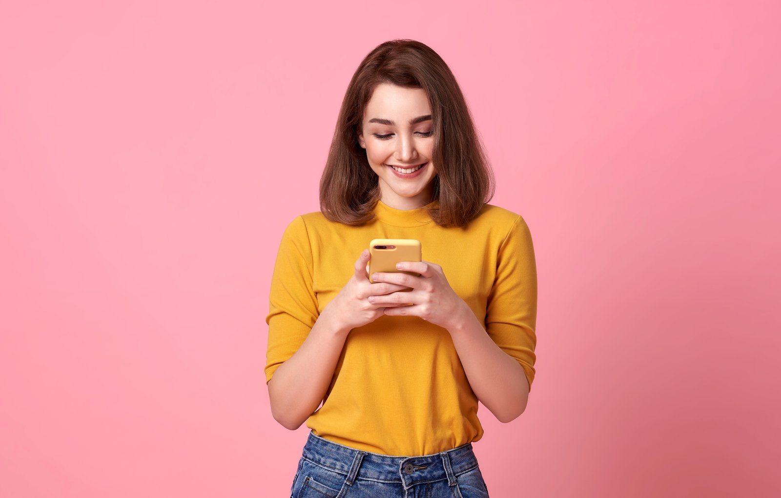 happy young woman good looking using mobile phone isolated pink space